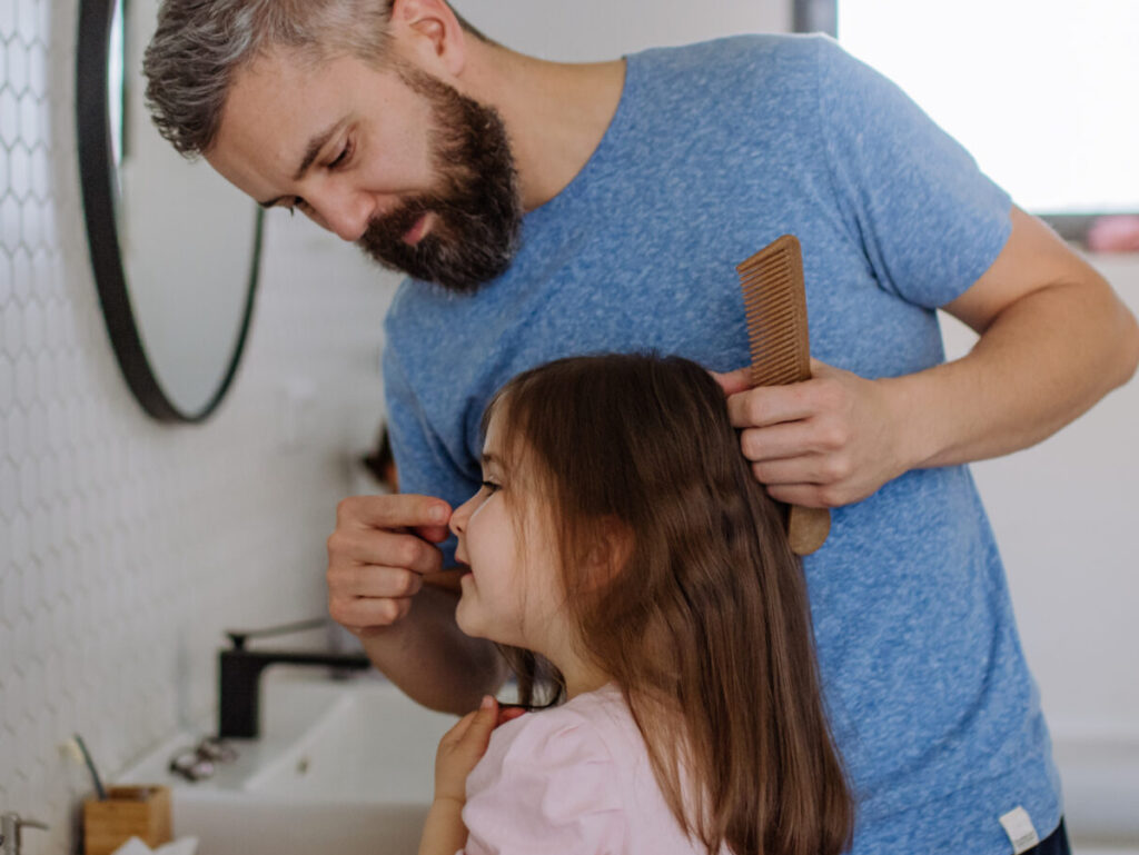 Father brushing his little daughter's hair in bathroom, morning routine concept.